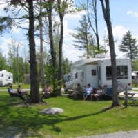Famille profitant d’un terrain boisé au Camping Magog Orford, roulottes et chaises longues à Orford en Estrie