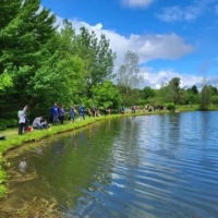 Familles pêchant au bord d’un plan d’eau entouré d’arbres, dans un cadre naturel et paisible au Camping Magog Orford en Estrie.