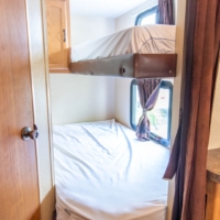 Lits superposés dans la roulotte Cruise Lite, avec matelas double en bas et lit simple en haut, près de deux fenêtres