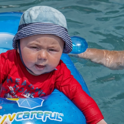 Bébé en gilet rouge flottant Bébé en gilet rouge flottant dans une piscine sur une bouée bleue, protégé du soleil par un chapeau à rayures, au Camping Magog Orford en Estrie